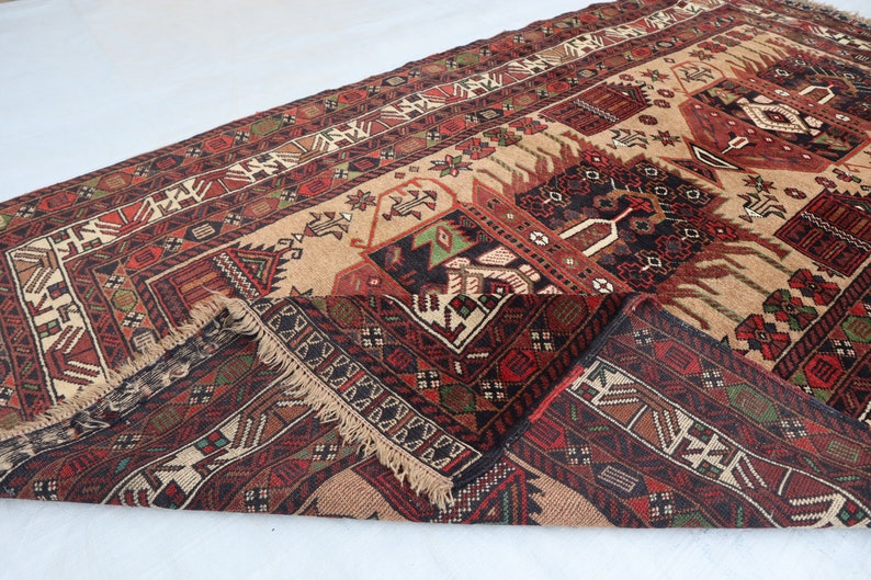 Pu&ograve; includere: Un tappeto tradizionale con sfondo beige e motivi intricati in tonalit&agrave; di rosso, nero e verde. Il tappeto ha un bordo con frange ed &egrave; piegato a met&agrave;.