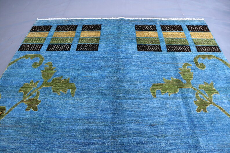 May include: A blue rug with a geometric pattern and floral designs. The rug has a light blue background with dark blue, green, and yellow accents.