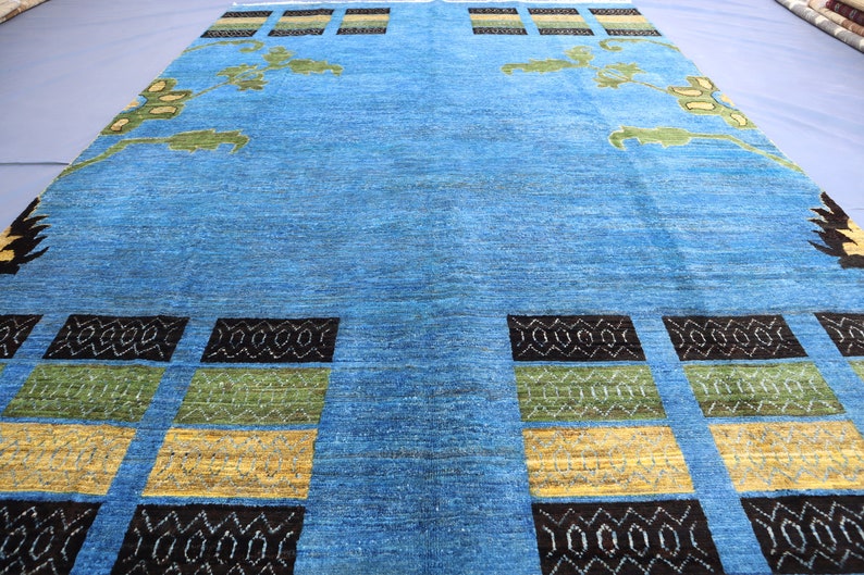 May include: A blue rug with a geometric pattern in black, green, and yellow. The rug has a floral design in the center.