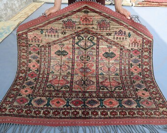 Puede incluir: Una alfombra de oración turca tradicional con fondo beige y intrincados patrones en rojo, azul y verde. La alfombra tiene un borde con flecos y está doblada por la mitad.