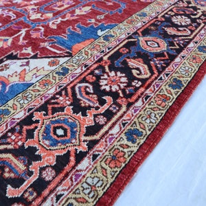 May include: Close-up of a red, blue, and cream colored rug with intricate floral patterns. The rug has a black border with a repeating design of stylized flowers and leaves.