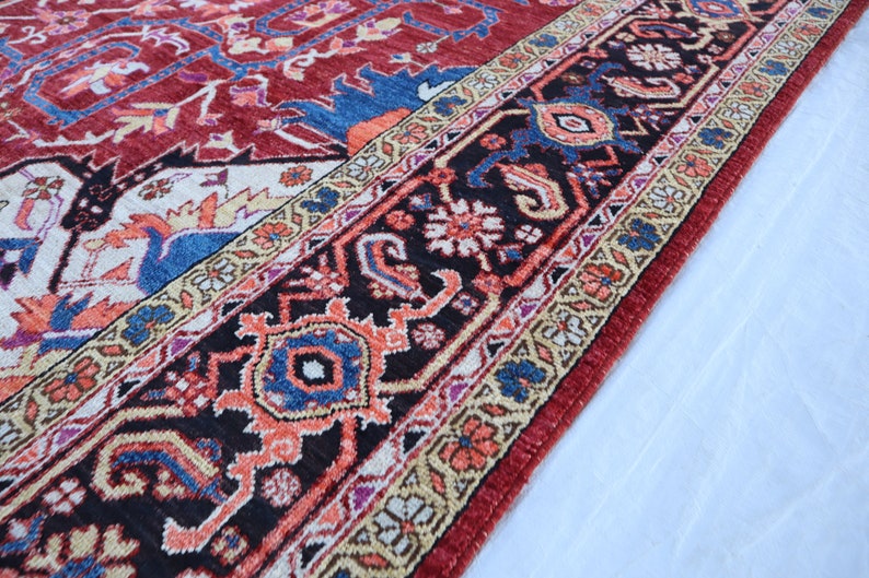 May include: Close-up of a red, blue, and cream colored rug with intricate floral patterns. The rug has a black border with a repeating design of stylized flowers and leaves.