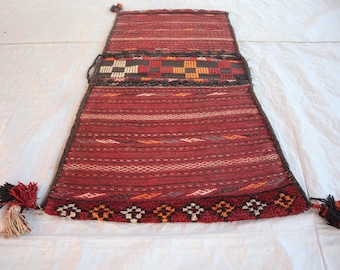 May include: A red, white and black patterned rug with fringe tassels on each end. The rug has a geometric design and is made of woven fabric.