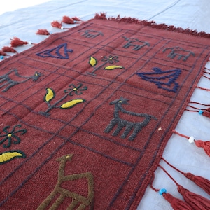 May include: A red woven rug with a geometric pattern of animals and flowers. The rug has fringe on all sides.