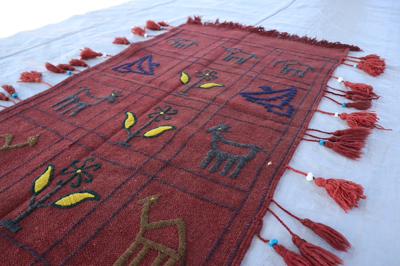 May include: A red woven rug with a geometric pattern of animals and flowers. The rug has fringe on all sides.