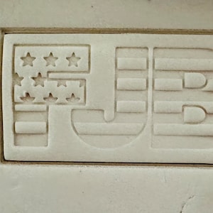 May include: A white rectangular stamp with the letters "FJB" in a stylised font. The "F" is a stylised American flag with red and white stripes and white stars.
