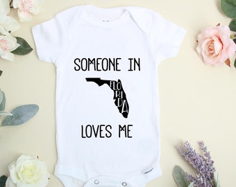 Könnte beinhalten: Weißer Baby-Strampler mit schwarzem Text, der "Jemand in Florida liebt mich" lautet. Der Text befindet sich innerhalb der Umrisse des Bundesstaates Florida.