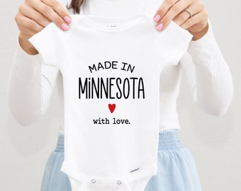 May include: White baby onesie with black text that reads "Made in Minnesota with love." A red heart is above the word "love."