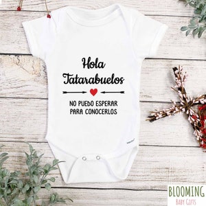 May include: White baby onesie with black text that reads "Hola Tataraabuelos" with a red heart and arrows pointing to the left and right. The text below reads "No puedo esperar para conocerlos".
