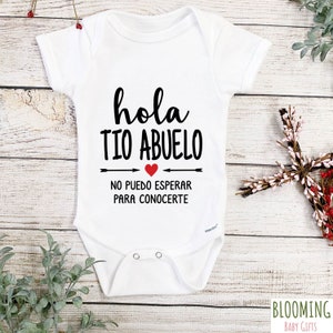 May include: White baby onesie with black text that reads "hola tio abuelo" with a red heart and the text "no puedo esperar para conocerte" below.