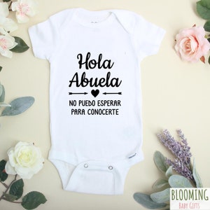 May include: White baby onesie with black text that reads "Hola Abuela" with a heart and arrows, and "No puedo esperar para conocerte".