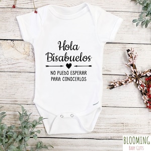 May include: White baby onesie with black text that reads "Hola Bisabuelos" with a heart and arrows above the text and "No puedo esperar para conocerlos" below the text.