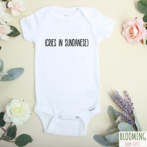 May include: White baby onesie with the text "(CRIES IN SUNDANESE)" printed in black.