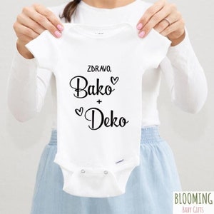 May include: White baby onesie with black text that reads "Zdravo, Bako + Deko" with hearts.