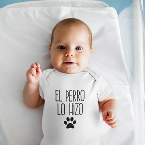 Könnte beinhalten: Ein Baby trägt einen weißen Strampler mit dem Text "EL PERRO LO HIZO" und einem schwarzen Pfotenabdruck.