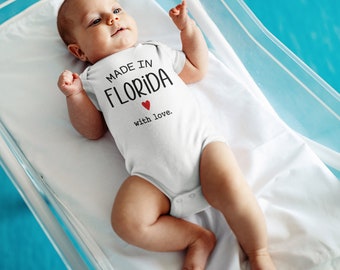 Könnte beinhalten: Ein weißer Baby-Strampler mit dem Text "Made in Florida with love." und einem roten Herzen.