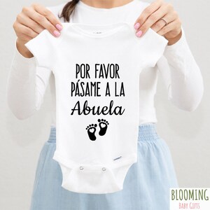Könnte beinhalten: Weißer Baby-Strampler mit schwarzem Text, der "Por favor pásame a la Abuela" lautet, mit einem Paar schwarzer Fußabdrücke mit Herzen in der Mitte.