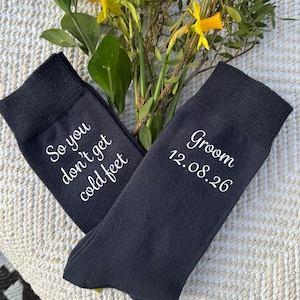 May include: A pair of dark blue socks with white text. One sock says "So you don't get cold feet" and the other says "Groom 12.08.26".