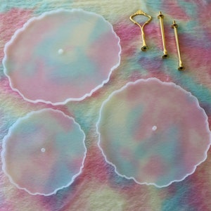 Può includere: Un set di vassoi da portata a tre livelli con un design tie-dye pastello. Il set include tre vassoi rotondi con bordi smerlati di diverse dimensioni e hardware color oro per l'assemblaggio. I vassoi hanno un bordo bianco e un foro centrale per l'hardware.