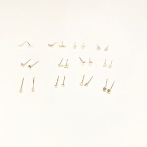 Pu&ograve; includere: Un set di 18 orecchini a perno d'argento con varie forme, tra cui cerchi, stelle, triangoli e quadrati. Gli orecchini sono disposti in file su uno sfondo bianco.