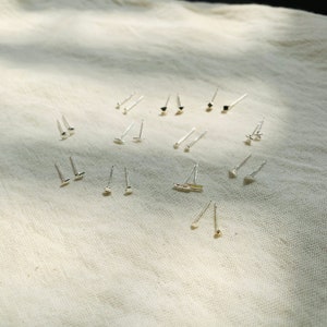 Pu&ograve; includere: Una collezione di orecchini d'argento con varie forme geometriche, tra cui quadrati, triangoli e cerchi, disposti su uno sfondo di tessuto bianco.