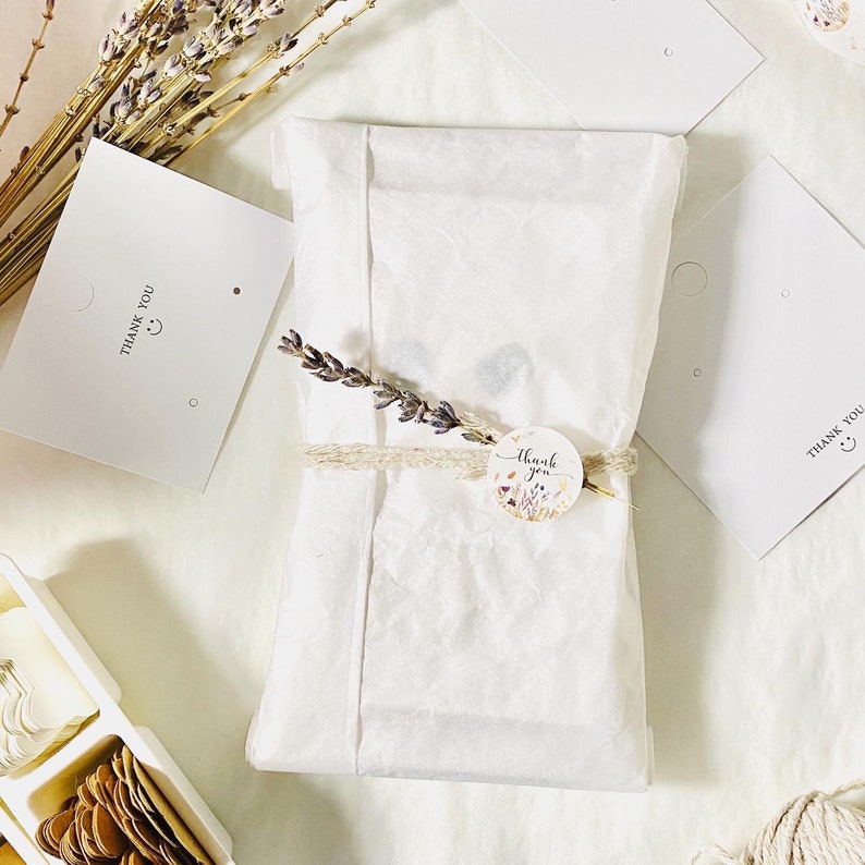 Pu&ograve; includere: Un pacchetto di carta velina bianca con un piccolo adesivo floreale che dice "Grazie" in scrittura marrone. Il pacchetto &egrave; legato con uno spago di iuta marrone e ha un rametto di lavanda secca in cima.