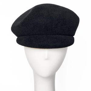 May include: A black beret hat with a rounded crown and a structured brim. The hat is displayed on a white mannequin head against a white background. The beret is made of a soft, textured material.