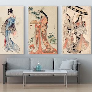 Könnte beinhalten: Drei gerahmte japanische Holzschnitte, die Frauen in traditioneller Kleidung zeigen. Die Drucke sind in Schwarz, Weiß und Schattierungen von Rosa, Blau und Grün gehalten. Die Drucke hängen an einer weißen Wand über einem grauen Sofa.