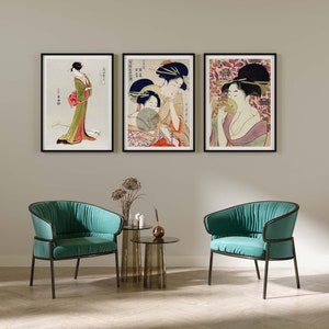 Könnte beinhalten: Drei gerahmte Drucke traditioneller japanischer Holzschnitte, die Frauen in farbenfrohen Kimonos darstellen. Die Drucke hängen an einer weißen Wand in einem modernen Wohnzimmer mit zwei türkisfarbenen Sesseln und einem Glas-Couchtisch.