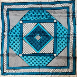 Peut inclure: Un foulard en soie bleu et blanc à motif géométrique. Le foulard présente une grande forme de diamant au centre avec un plus petit diamant à l'intérieur. L'arrière-plan est un motif à carreaux blancs et gris.