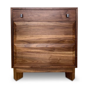 May include: A three-drawer wooden dresser with a walnut finish. The dresser has two small drawers and one large drawer. The drawers have simple metal pulls.