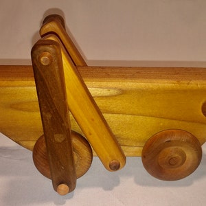 May include: A wooden toy wagon with a brown wooden handle and two brown wooden wheels. The wagon has a rope attached to the back for pulling.
