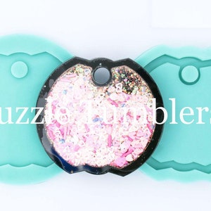May include: Two turquoise silicone molds for making round keychains with a hole at the top. The molds are 2 inches in diameter. A finished keychain with a glittery design is shown in the center.