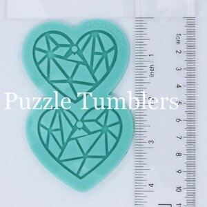 May include: Two turquoise silicone molds shaped like hearts with a geometric pattern inside. The molds are 5 inches tall and are next to a ruler for size reference. The text "Puzzle Tumblers" is printed on the top mold.
