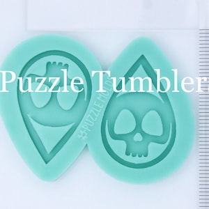 May include: Two teal blue silicone molds for resin crafts. One mold is shaped like a teardrop and features a skull design. The other mold is shaped like a teardrop and features a stylized anchor design. The molds are next to a ruler for size reference.