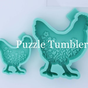 May include: Two teal silicone molds shaped like chickens with floral patterns inside. The smaller mold is approximately 3 inches tall, and the larger mold is approximately 4.5 inches tall, as shown by the clear plastic ruler placed to the right.