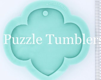 May include: A light blue silicone mold shaped like a four-leaf clover with a hole at the top for hanging. The mold is approximately 2 inches in diameter. The text "Puzzle Tumblers" is printed on the mold.