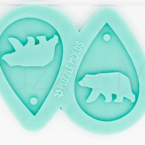 May include: Two teal blue silicone molds for making earrings. Each mold features a bear silhouette. The mold on the left has a mother bear with a cub. The mold on the right has a single bear walking. The molds are approximately 2 inches in length. #PuzzleMolds