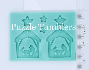 May include: A teal blue silicone mold with two nativity scene designs and two star shapes. The mold is approximately 2 inches wide and 3 inches tall. The text "Puzzle Tumblers" is printed on the mold.