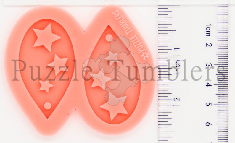 K&ouml;nnte beinhalten: Eine rosa Silikonform zum Herstellen von Ohrringen. Die Form hat zwei tropfenf&ouml;rmige Vertiefungen mit einem Sternmuster. Die Form ist 5 cm lang und 2,5 cm breit.