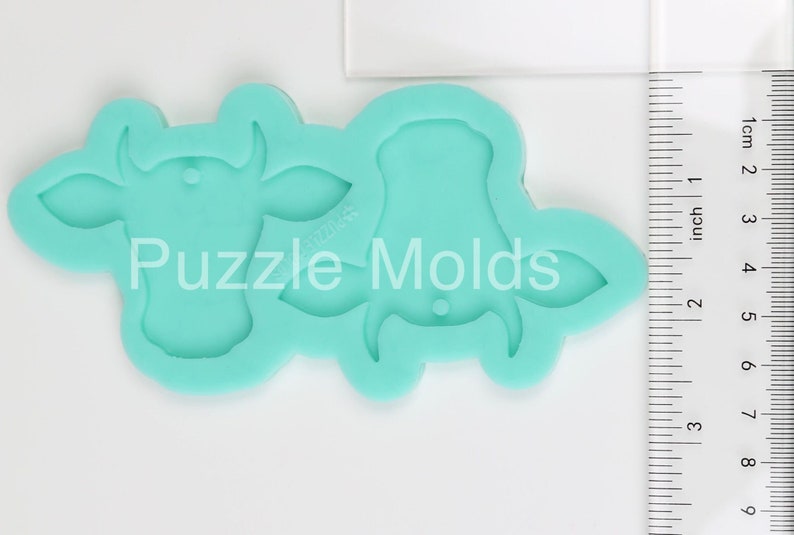 May include: A turquoise silicone mould for making two cow-shaped decorations. The mould is approximately 5 cm wide and 5 cm tall. The mould is made by Puzzle Molds.