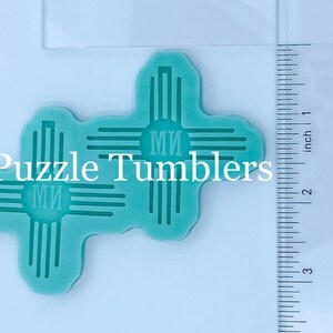 May include: Two turquoise silicone molds of the Zia symbol, a traditional symbol of the Pueblo people of New Mexico. The molds are approximately 2 inches in size and feature the text "Ми" in the center.