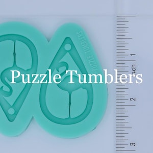 May include: A teal silicone mold for making earrings shaped like a flamingo. The mold is about 2 inches wide and 2 inches tall. The mold is next to a ruler for size reference.