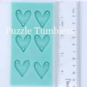 May include: A light green silicone mold with four heart-shaped cavities. Each heart has a different word inscribed in it: "BYE", "BYE", "TEX", and "TEX". The mold is 4 inches tall and 2 inches wide.