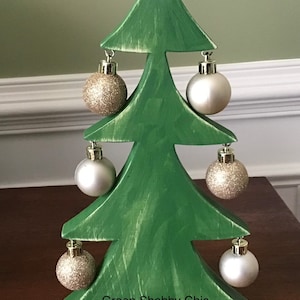 Könnte beinhalten: Ein grüner Weihnachtsbaum aus Holz mit sechs hängenden Ornamenten. Die Ornamente sind silber und gold mit Glitzer. Der Baum ist im Shabby-Chic-Stil bemalt und trägt am Boden die Aufschrift "Green Shabby Chic".