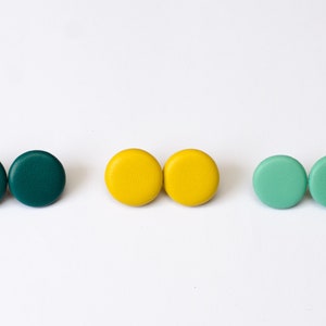 Puede incluir: Tres pares de pendientes redondos de botón en color verde azulado, amarillo y verde menta.