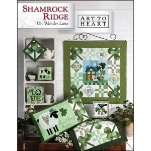 May include: A green and white quilt with a shamrock design and the words "Shamrock Ridge On Wander Lane" and "Art to Heart". The quilt is displayed on a white shelf with other green and white decorations.