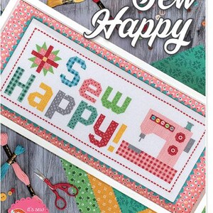 May include: A framed cross-stitch design with the words "Sew Happy" in colorful letters. The design includes a pink sewing machine and a floral pattern. The background features sewing supplies like thread, scissors, and buttons.