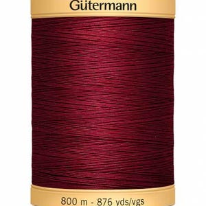 Puede incluir: Una bobina de hilo Gütermann de color burdeos. La etiqueta beige muestra el nombre de la marca y el texto "800 m - 876 yds/vgs". El hilo está bien enrollado, mostrando la textura de las fibras. Suministros de costura.