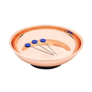May include: A copper-colored magnetic pin dish with three blue-tipped pins inside.